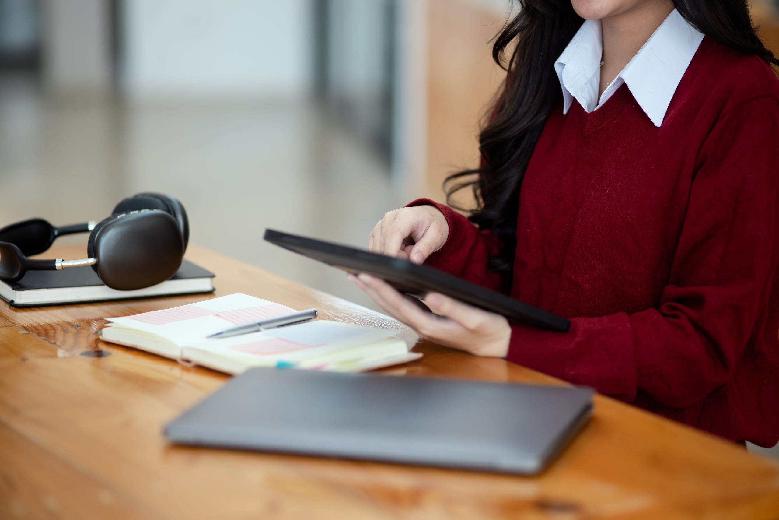 Happy young asian woman wearing earphones and using laptop computer at desk in office, Female student with stack of books and laptop.